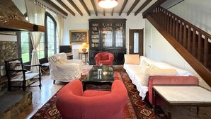 A cozy living room with a fireplace, a red armchair, a white sofa, and a wooden staircase. - Bernet - Labastide-villefranche (LABASTIDE-VILLEFRANCHE)