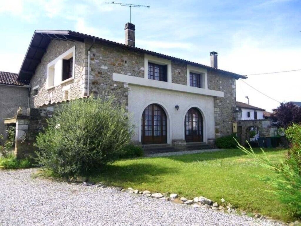 A stone house with a white facade, two arched windows, and a gravel driveway.