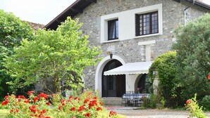 A stone building with a white facade, a covered patio with outdoor seating, and a garden with red flowers. - Bernet - Labastide-villefranche (LABASTIDE-VILLEFRANCHE)