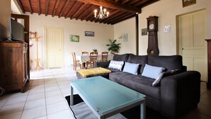 A living room with a dark sofa, a glass coffee table, a wooden cabinet, a dining table with chairs, and a chandelier. - Chez Laborde - Riupeyrous (RIUPEYROUS)