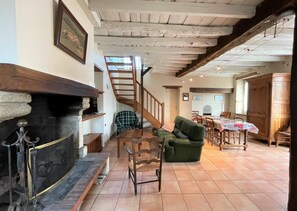 Un intérieur rustique avec une cheminée, un canapé vert, un coin repas et un escalier.