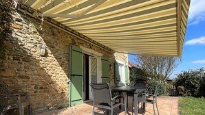 A patio area with a stone wall, a covered table with chairs, and a green door. - Chez Evon - Jurancon (JURANCON)