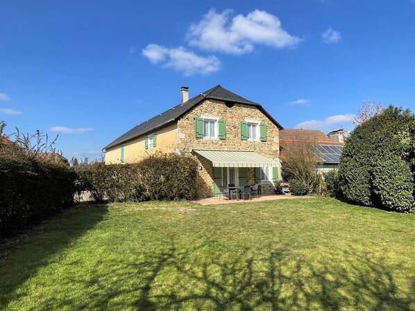 A stone house with a green roof, a covered patio, and a well-maintained lawn. - Chez Evon - Jurancon (JURANCON)