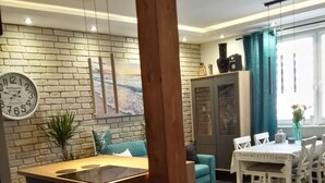 Une cuisine moderne dotée d’un îlot central, d’un coin repas avec une table et des chaises, et d’un mur en briques orné d’une horloge.