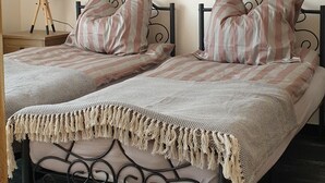 Un lit double avec une literie à rayures et un couvre-lit en macramé, une table de chevet avec une lampe, et un tableau représentant un navire accroché au mur.