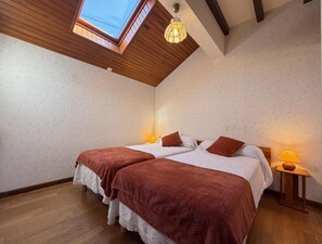 Un dormitorio con dos camas, vigas de madera, un tragaluz y una lámpara colgante.