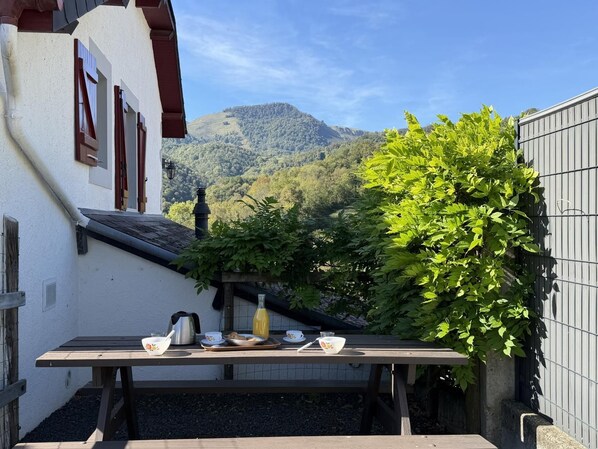 Ein Holztisch mit Frühstücksangeboten und einer Flasche vor einer Bergkulisse.