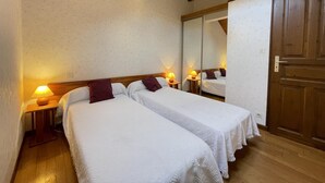 Une chambre avec deux lits, des poutres en bois au plafond, un grand miroir et une porte en bois.