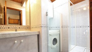 Un baño con lavadora, cabina de ducha de vidrio y lavamanos de mármol.