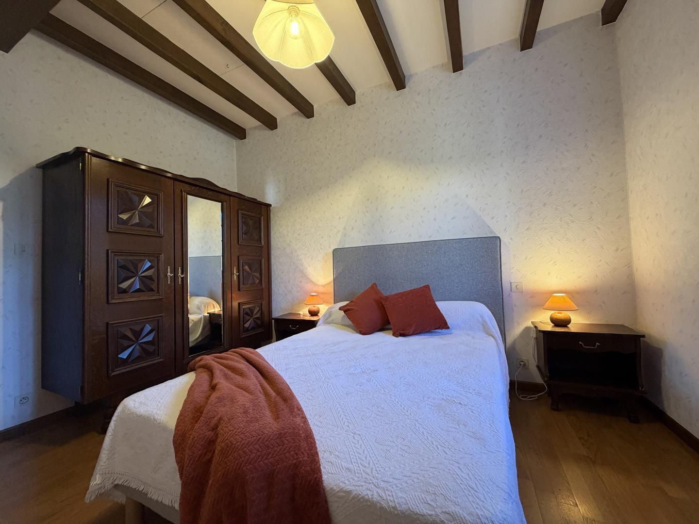 Een slaapkamer met een bed, een houten garderobe en twee bedlampjes.