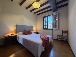 Ein Schlafzimmer mit Bett, Nachttischen, einem Sessel, einem Fenster und einer Pendelleuchte.