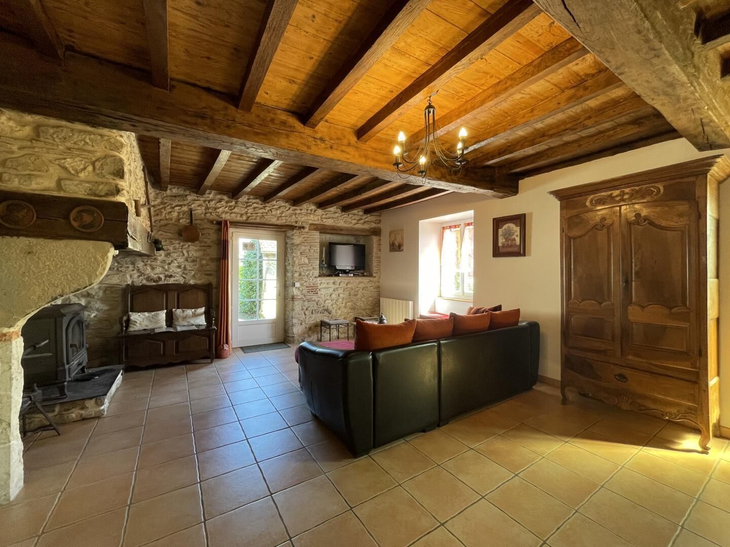 Un intérieur rustique avec des poutres apparentes, une cheminée en pierre, un canapé et une armoire en bois.