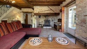 Un salon chaleureux avec une cheminée en pierre, des poutres en bois et un canapé agrémenté de coussins à rayures.