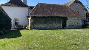 Un bâtiment en pierre avec un toit recouvert de tuiles, une cheminée et une petite porte.