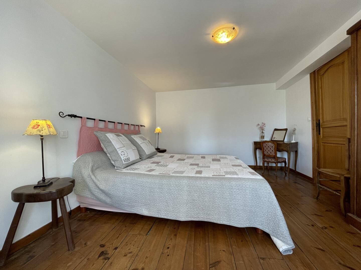 A bedroom with a bed, two bedside lamps, a wooden chair, a desk, and a wardrobe.