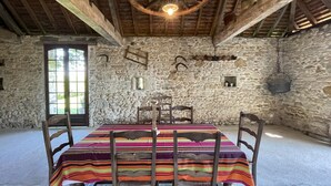 Une salle à manger rustique avec un mur en pierre, des poutres en bois et une grande table en bois entourée de chaises.