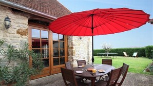 Un espace de restauration en plein air avec un bâtiment en pierre, un parasol rouge et une vue sur le jardin.