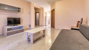 A modern living room with a flat-screen TV, a white coffee table, a grey sofa, and a wooden chair.