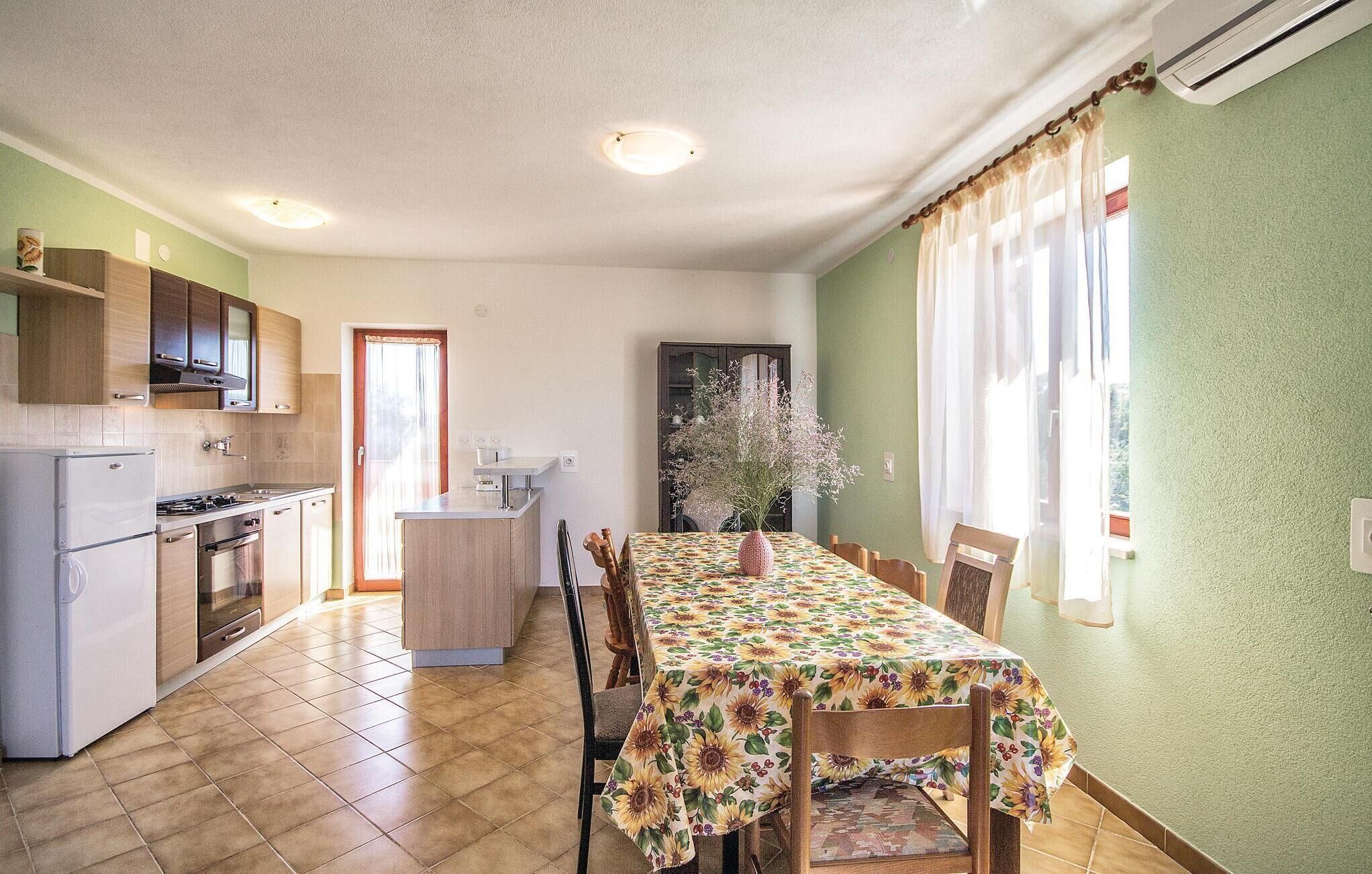 A compact kitchen with a dining area, featuring a tiled floor, wooden cabinets, and a table with a floral tablecloth.