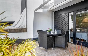 En udendørs terrasse med fletningsmøbler, et bord og krukker med planter.