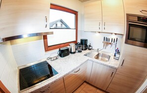Compact kitchen with electric stove, coffee maker, and toaster, offering a view of the surrounding house.