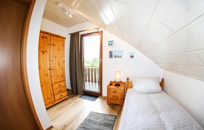 Cozy bedroom with a sloped ceiling, wooden wardrobe, and a comfortable bed with a bedside table and lamp.