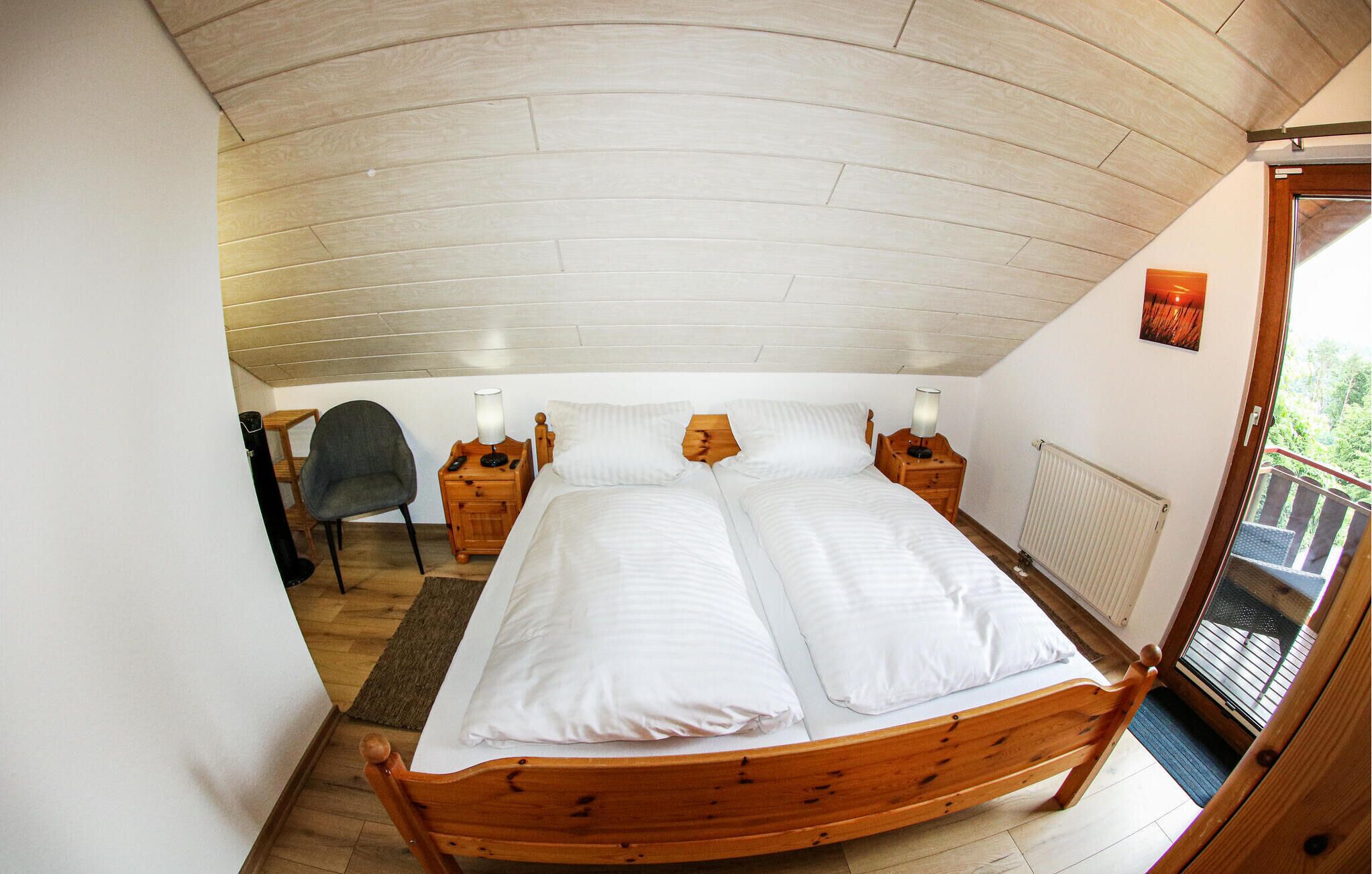 A bedroom with a wooden bed, two bedside tables with lamps, a chair, and a view of the outdoors through a window.