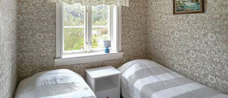 Un dormitorio con dos camas individuales, una mesita de noche, un ventanal con vistas a zonas verdes y un cuadro en la pared.