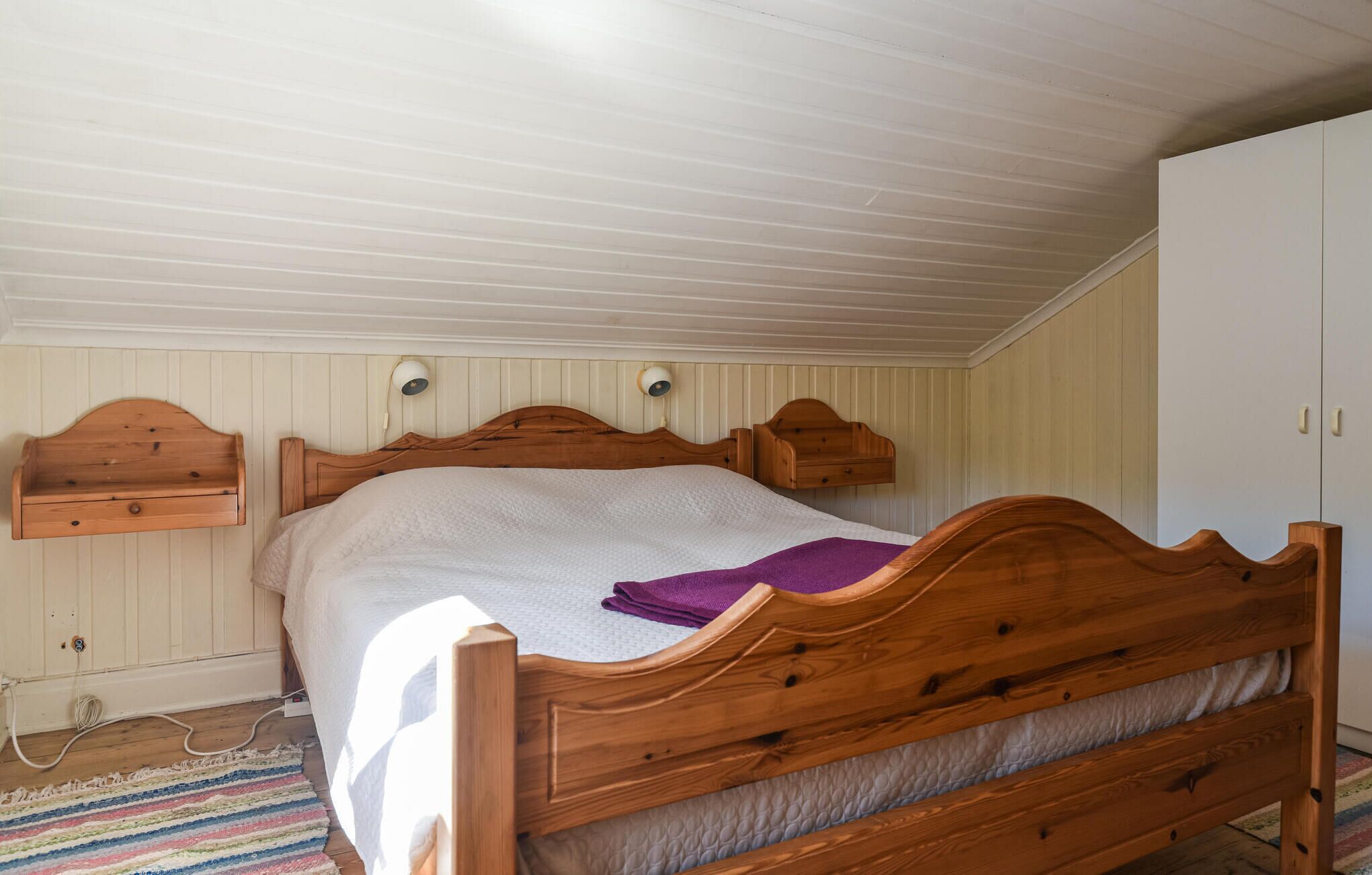 A single bed with a wooden headboard and footboard, a white wall with wooden paneling, and a small bedside table with a lamp.