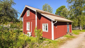 A red wooden house with a sloped roof, a small porch, and a dirt path leading to it. - Nice home in Munkedal with lake view (Munkedal)