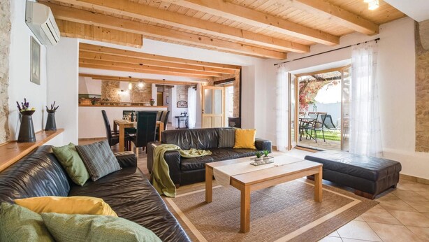 Ein geräumiges Wohnzimmer mit Holzboden, einer Sofagarnitur, einem Couchtisch und Blick auf den Garten durch eine Glastür.