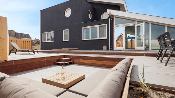 A modern outdoor living area with a wooden deck, built-in seating, and a glass door leading to a covered patio. - Awesome home in Bergen aan Zee (Bergen aan Zee)