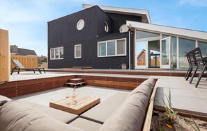 Een moderne buitenruimte met een houten terras, ingebouwde zitplaatsen en een glazen deur naar een overdekt terras.