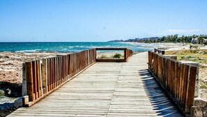 A wooden boardwalk leading to a beach with a clear view of the ocean and distant buildings. - Gorgeous apartment in Cabanes with swimming pool (Cabanes)