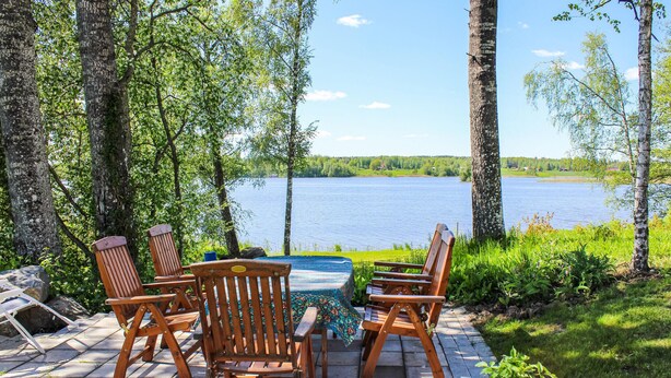 An outdoor seating area with wooden chairs and a table, overlooking a lake.
