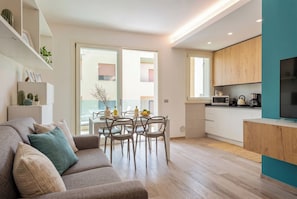 A modern living room with a sofa, dining table, chairs, and a kitchen area with cabinets and appliances.