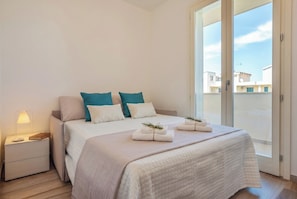 A bedroom with a bed, pillows, a nightstand, a lamp, and a view through a glass door.