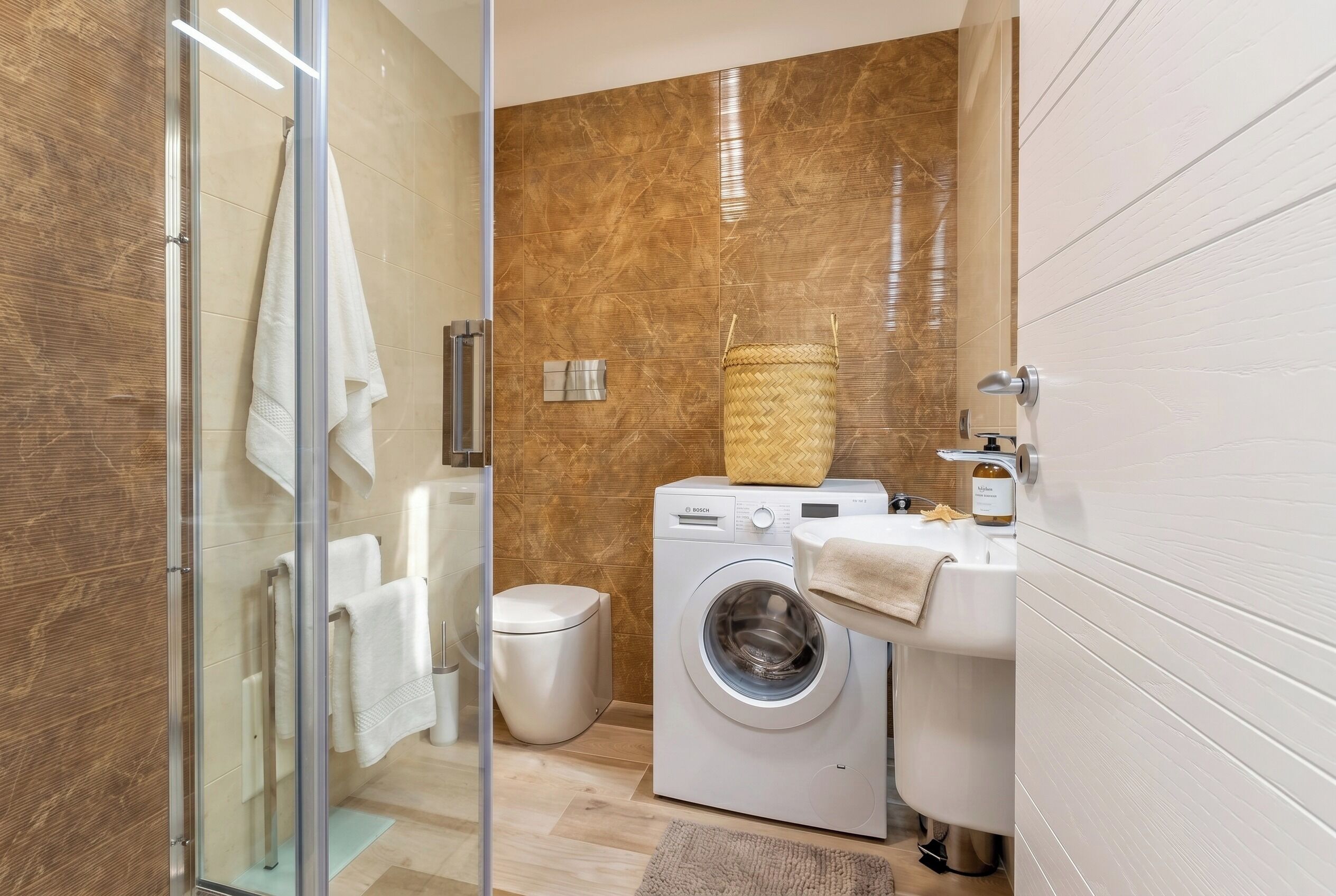 Een moderne badkamer met een douchecabine van glas, een Bosch wasmachine, een wastafel en een toilet.