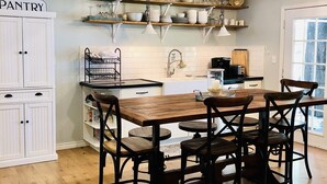 Une cuisine avec une table et des chaises en bois, des meubles de rangement blancs et un espace garde-manger.