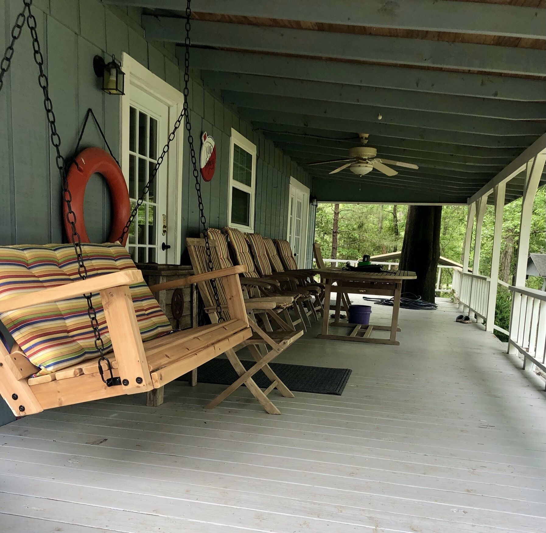 A porch with wooden chairs and a swing, a table, and a ceiling fan.