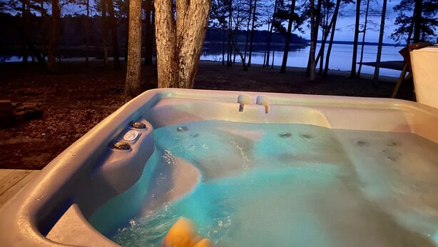Un bain à remous avec vue sur un lac et des arbres, au crépuscule.