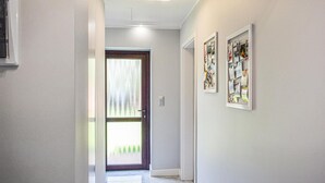 Een gang met een deur naar een kamer, een lamp aan het plafond en twee ingelijste foto's aan de muur.