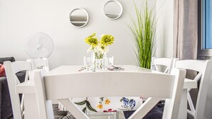 Een eetgedeelte met een ronde tafel, witte stoelen, een ventilator en een vaas met gele bloemen.