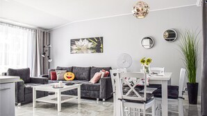Een moderne woonkamer met een grijze bank, een witte salontafel en een eethoek met een witte tafel en stoelen.