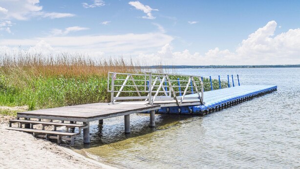 Een houten steiger die zich uitstrekt over een wateroppervlak, met een metalen reling en trappen die naar een aanmeerplaats leiden.