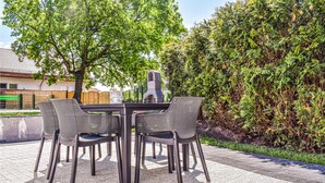 Een terras buiten met een tafel en stoelen, omringd door groen en een stenen muur.