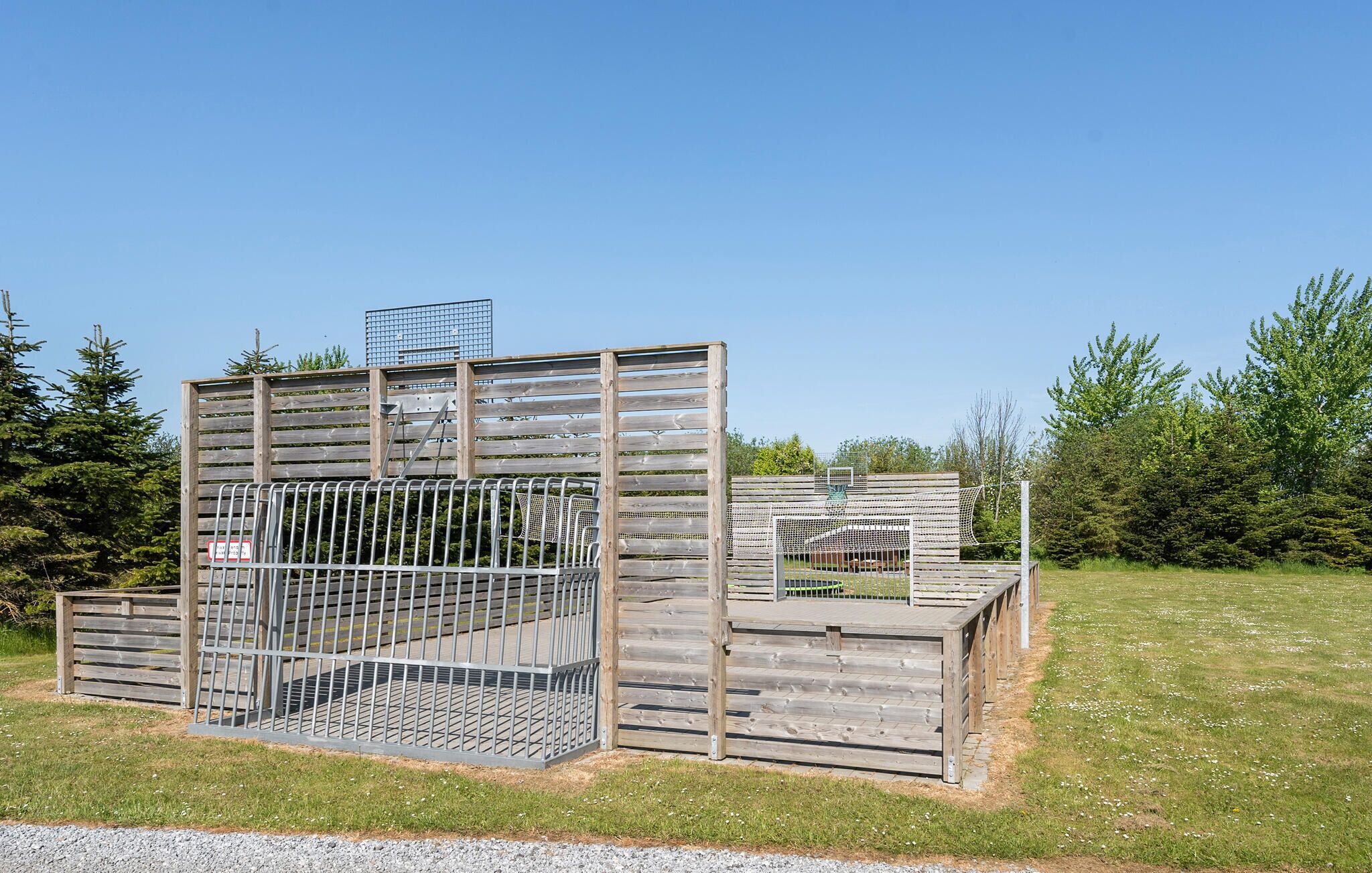 A wooden structure with metal mesh and a ladder, surrounded by greenery.