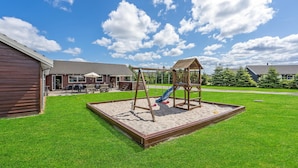 Een speeltuin met een schommel en glijbaan, omringd door een houten terras en een gazon.
