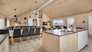 Een ruime keuken met een centraal eiland, een eethoek met stoelen, en een woonruimte met een bank en televisie.