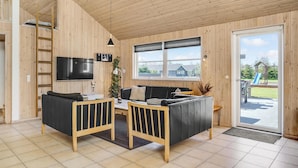 Een gezellig interieur van een chalet met houten details, een televisie aan de muur, een bank en een eettafel.